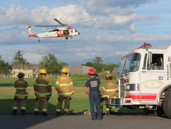 WCFD7 personnel watch as NAS Whidbey Island S&R crews simulate a rescue via helicopter at the Mountain View school campus (June 12, 2017). Photo: Whatcom News