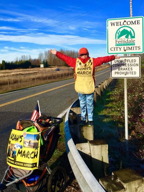 noah barnes poses by a Ferndale city limit sign on the last day of his cross country trek photo via fb
