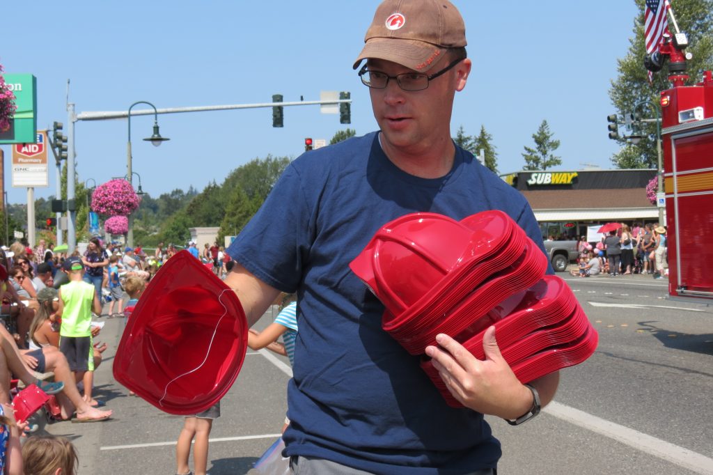 A helper with the Cherry Point Refinery Emergency Response entry in the 2018 Whatcom Old Settlers Grand Parade in Ferndale hands out toy firefighter helmets (July 28, 2018). Photo: My Ferndale News