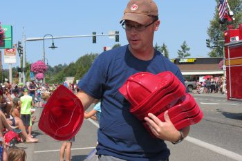 A helper with the Cherry Point Refinery Emergency Response entry in the 2018 Whatcom Old Settlers Grand Parade in Ferndale hands out toy firefighter helmets (July 28, 2018). Photo: My Ferndale News