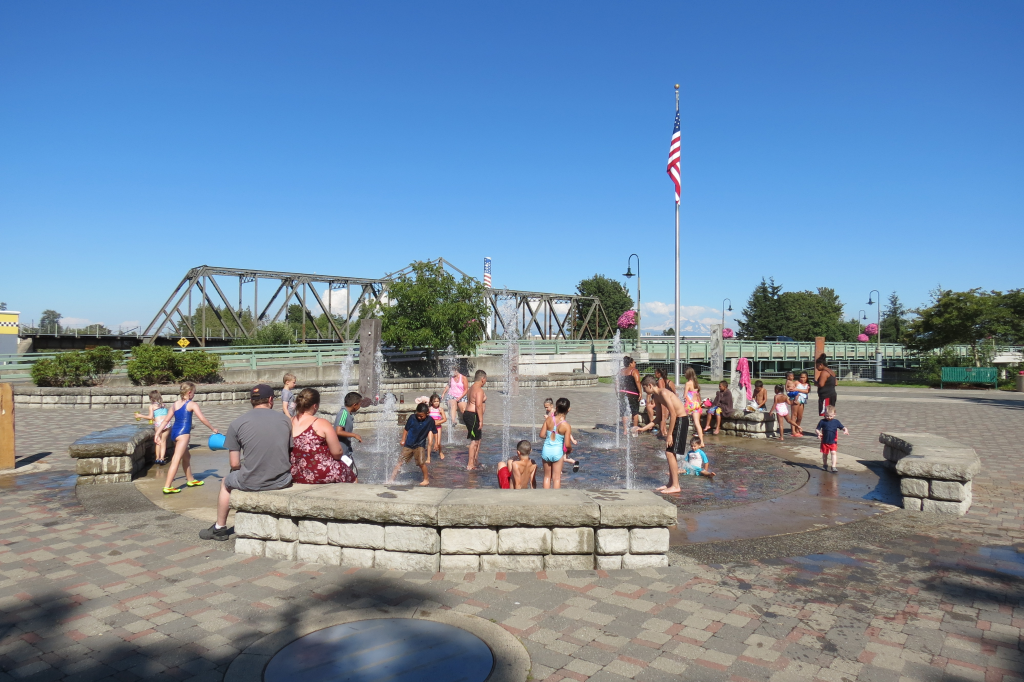 Families enjoy the fountain at the Centennial Riverwalk during warm weather with highs in the 80s (July 23, 2018). Photo: Whatcom News