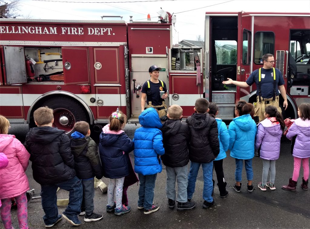 Bellingham Firefighter Jeff Heinrichs (right) speaks to a group of Central Elementary students after they received free coats from the Operation Warm program and IAFF local 106 (December 6, 2019). Photo: Whatcom News