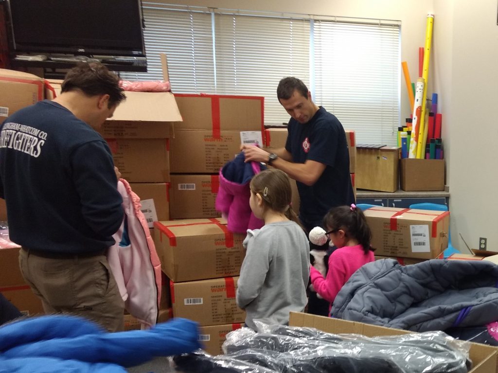 Bellingham/Whatcom County Firefighter volunteers help Central Elementary students pick a new coat during Operation Warm (December 6, 2019). Photo: Whatcom News