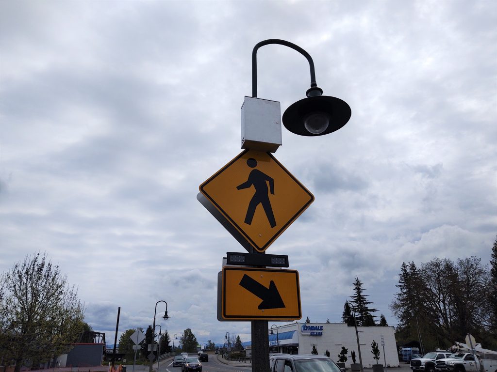Signs with a rectangular rapid flash beacon (RRFB) mounted on a light pole at 1st Avenue and Main Street (April 24, 2020). Photo: My Ferndale News