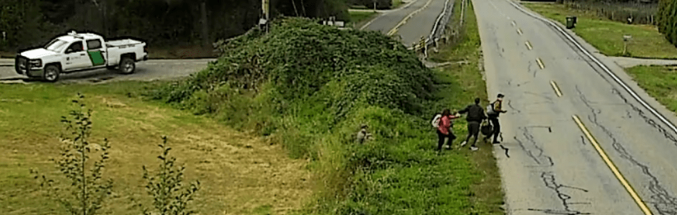 3 people are seen crossing the US-Canada border while being pursued by a US Customs and Border Protection officer. Source: BC RCMP